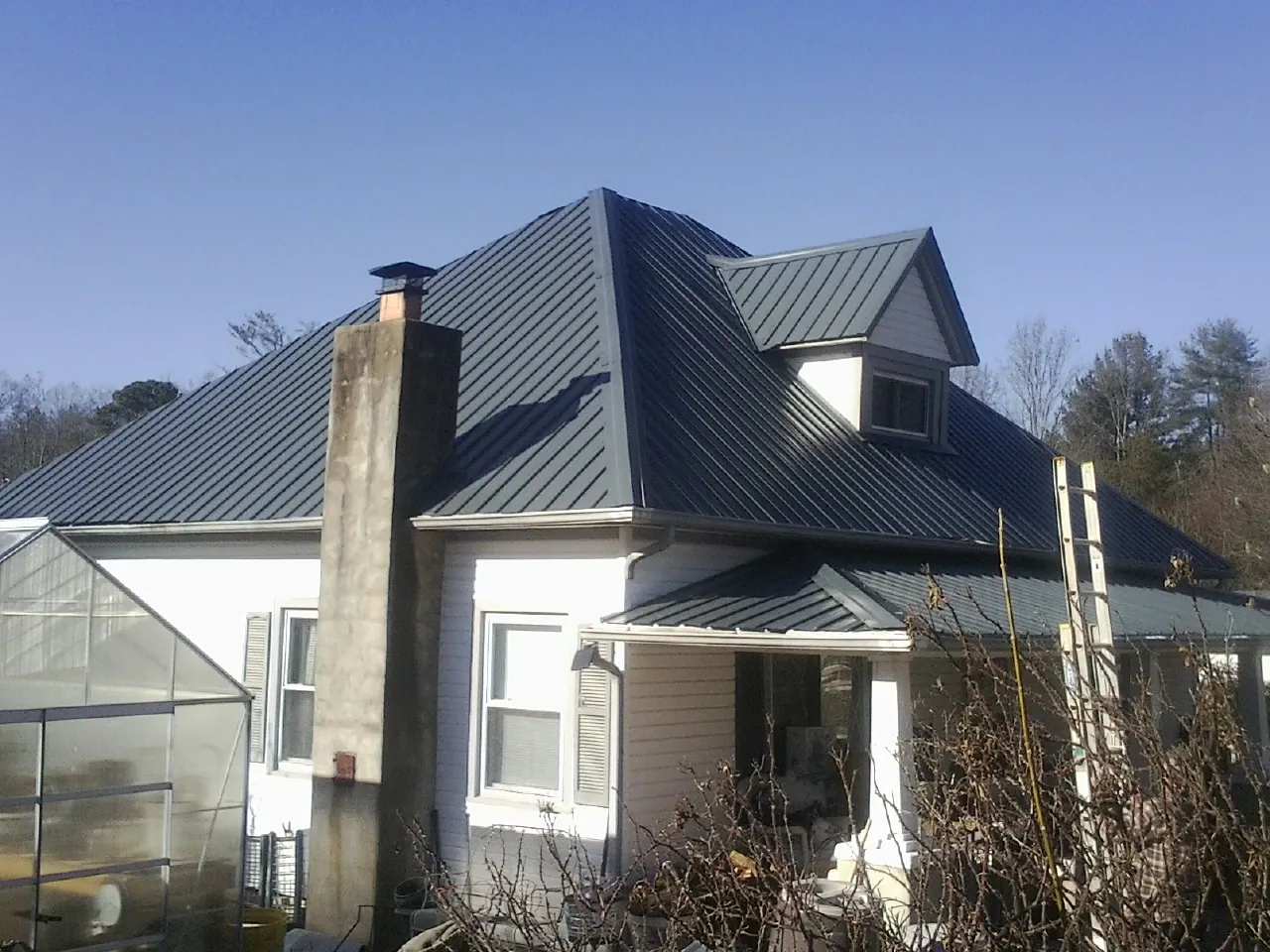 Dark blue standing seam metal roof on a white farmhouse with dormer — Slate & Tile Roof Repair by Roofing Brothers in Westley