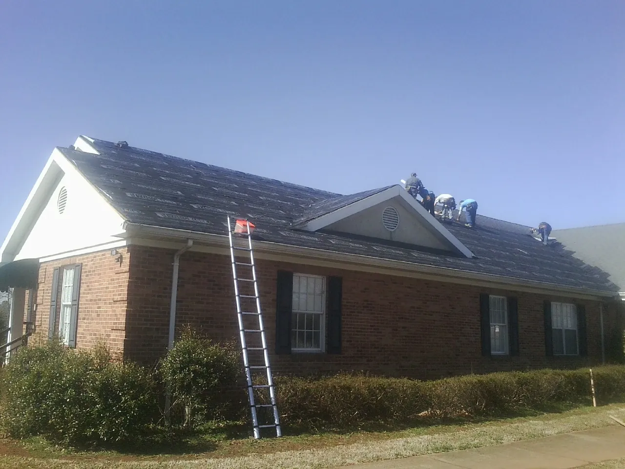 Crew tearing shingles off a brick ranch roof with a ladder set — Metal Roof Repair work by our crew in Westley