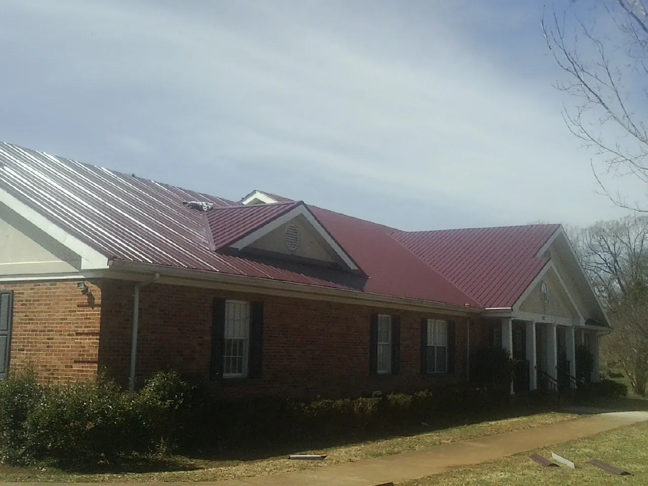 Red metal roof with gabled entries on a long brick building, from a Hail Damage Roof Repair job in Westley