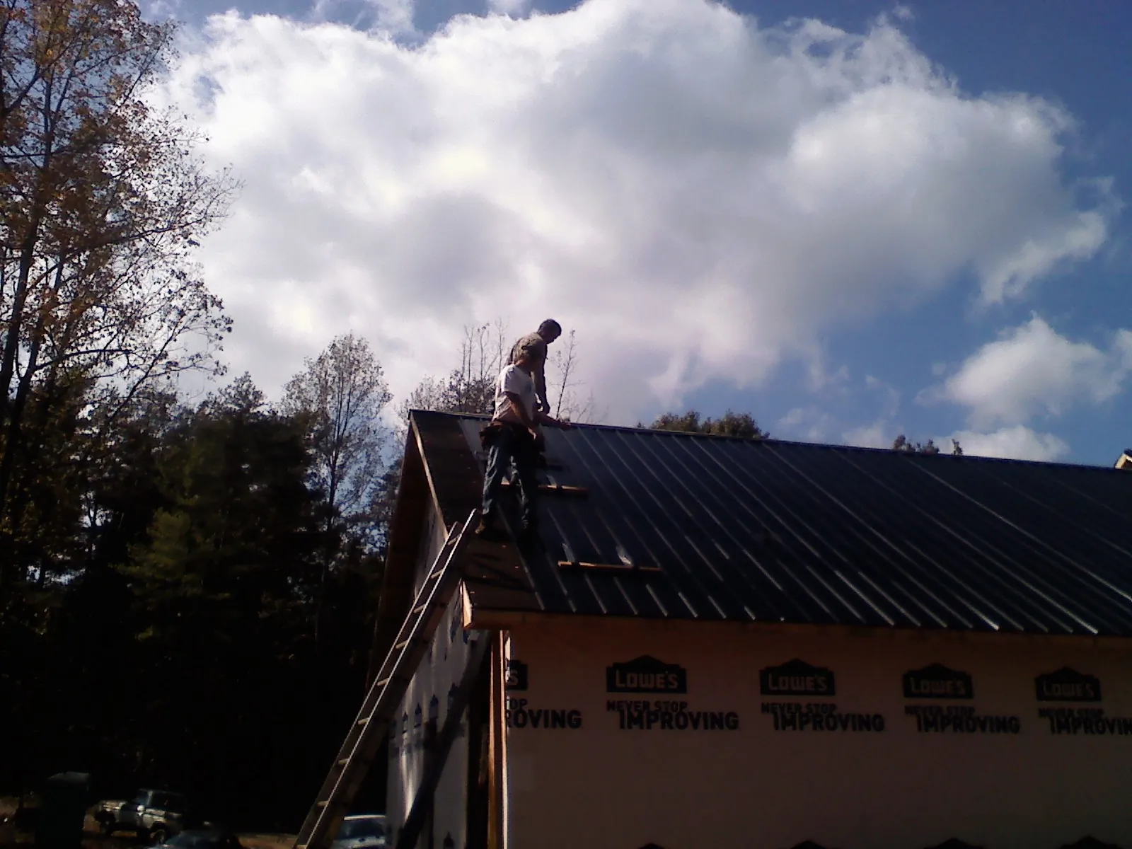 Roofer fastening dark metal panels high against a cloudy sky, from a Roof Inspection job in Westley