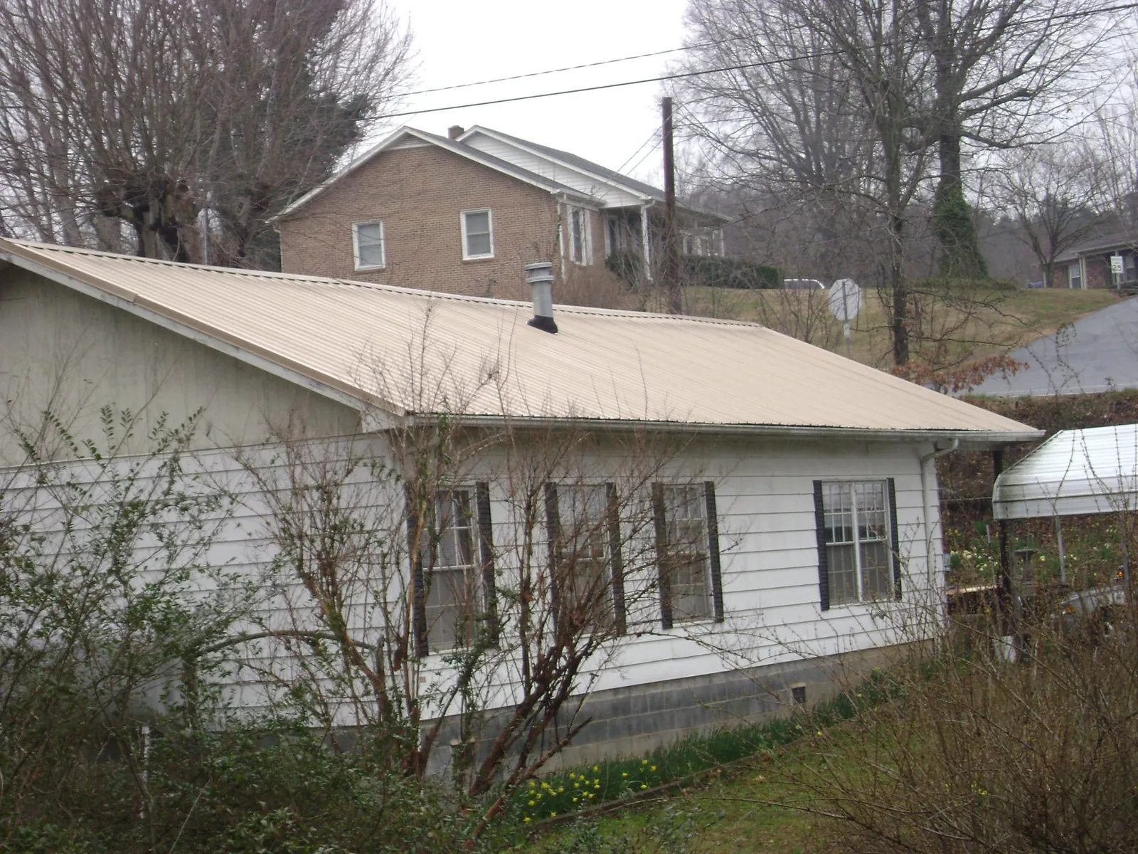 Tan metal roof on a white sided house set into a hillside — Commercial Roofing by Roofing Brothers in Westley