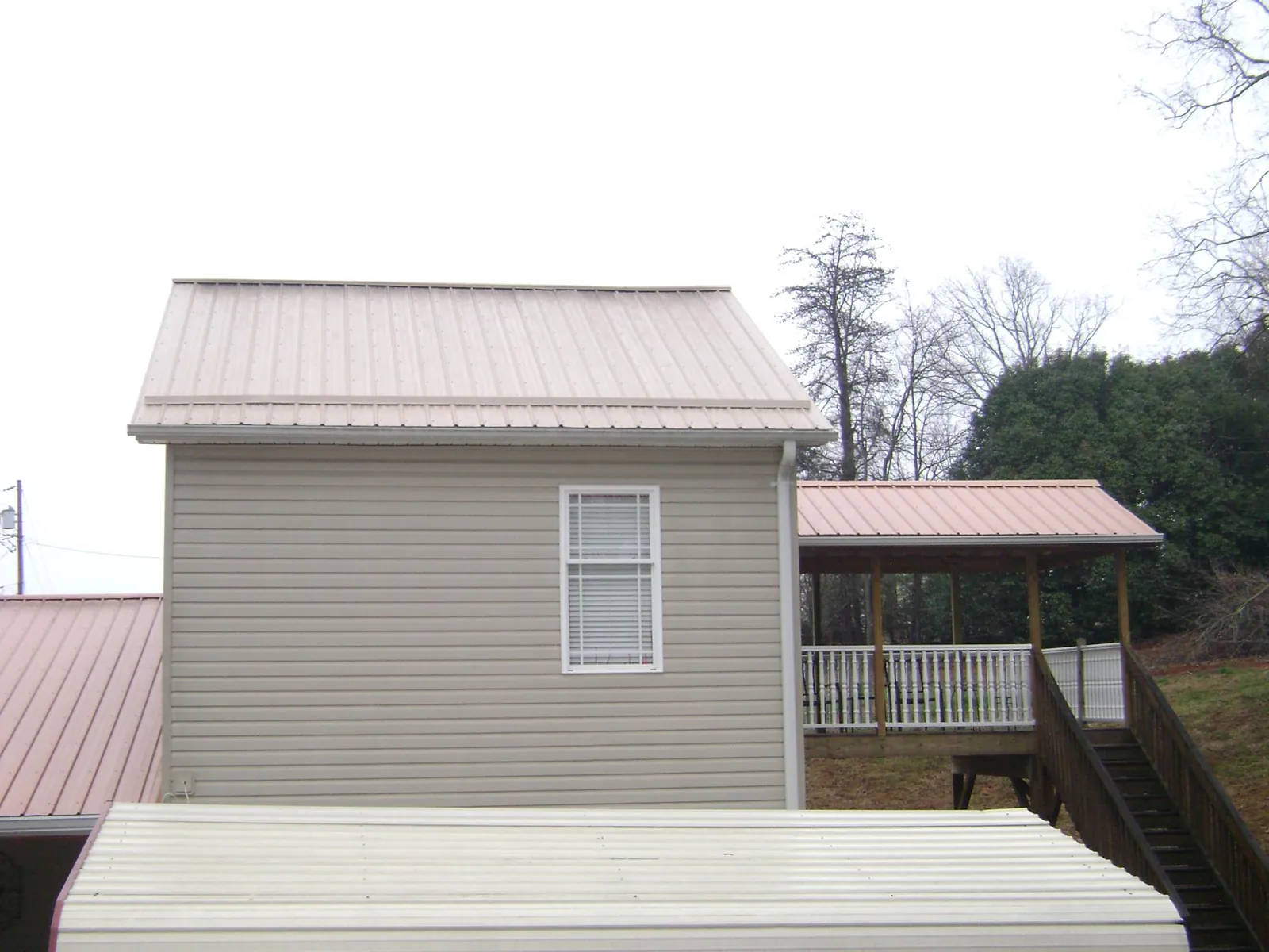 Tan metal roofs on a two story addition and attached porch, from a Roof Replacement job in Westley